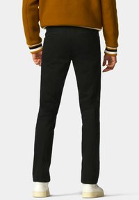 Zwarte broek met een slim fit, voorzien van achterzakken en een omgerolde zoom, gecombineerd met witte sneakers en een oranje trui.