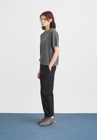 Pelēks īsām piedurknēm krekls, brīvas formas, saskaņots ar melnajām biksēm un pelēkām pārgājienu kurpēm. Vienkāršs dizains, mīksta tekstūra un neitrālas krāsas.