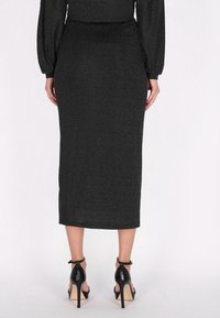 Czarna, ołówkowa spódnica do kolan o błyszczącej teksturze i subtelny połysk. Noszona z czarnymi butami na wysokim obcasie z paskami na kostkach.