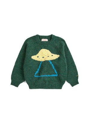 Garçon portant un pull vert avec un motif OVNI jaune, un pantalon à carreaux bleu et des mocassins foncés, debout devant un fond uni.