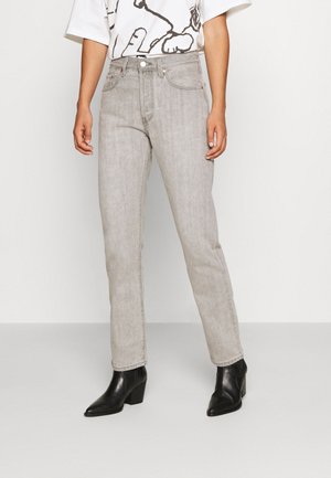 Personne portant un jean gris clair coupe droite, des bottines noires à talons et un t-shirt blanc avec un imprimé abstrait noir.