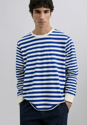 Camisa de manga larga a rayas en azul y blanco, hecha de suave algodón. Presenta un cuello redondo y puños acanalados, con un dobladillo redondeado.