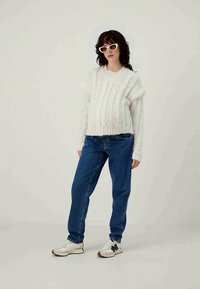 Kreemikas kudum sotsiaalne käik, mis on ühendatud siniste sirgete joontega teksade ja valgete tenistega tumeaktsentidega.