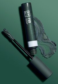 Grønn mascara i en sylinderformet tube med svart lokk. Inkluderer en applikator med piggete bust og en swatch av det grønne produktet ved siden av.