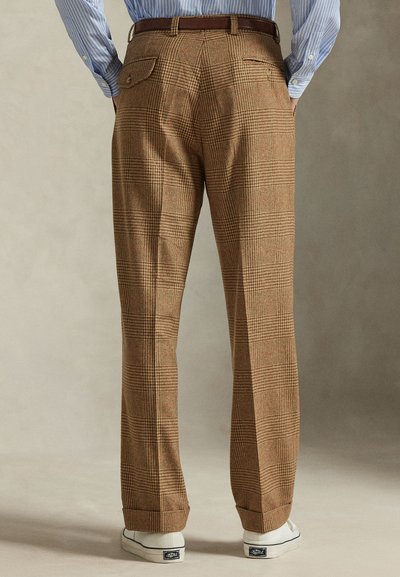 Καφέ καρό παντελόνι με υφή, διακοσμημένο με ίσια γραμμή σχεδίασης, πλαϊνές τσέπες και πίσω τσέπη, συνδυασμένο με λευκά αθλητικά παπούτσια.