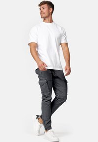 Grå cargobyxor med flera fickor, slim fit och anklar med dragkedjor, i kombination med en enkel vit T-shirt med kort ärm och vita sneakers.