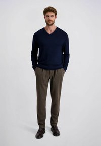 Marine V-hals trui, bruine gestructureerde broek en donkere schoenen. De outfit heeft een ontspannen pasvorm en een eenvoudig ontwerp.
