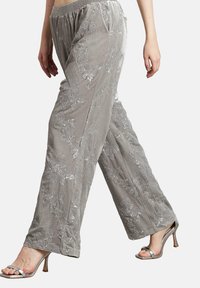 Pantalones de terciopelo gris con bordado de lentejuelas florales, cintura elástica, combinados con sandalias de tacón alto con los dedos al aire de color plateado.