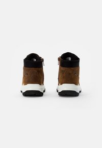 Stivaletti in suede marrone con colletto in tessuto nero e suola in gomma bianca, dotati di chiusura con zip e dettagli testurizzati sui lati.
