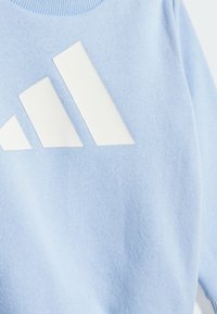 Sweatshirt bleu clair en tissu doux avec un grand design graphique à trois bandes blanches. Texture lisse avec un col rond.