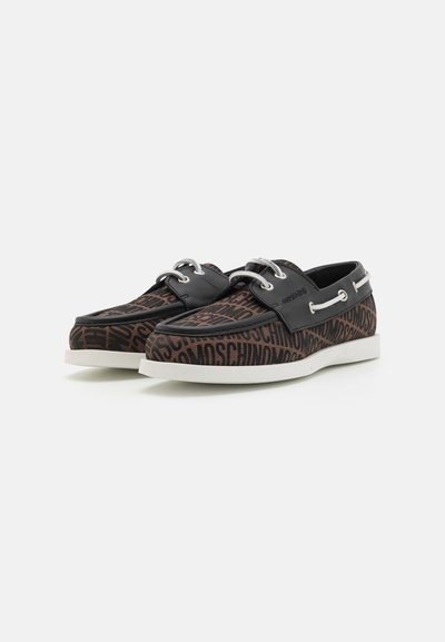 Zapatos con un patrón negro y marrón, con un upper de lona, que presentan ojales plateados, una suela blanca y detalles de cuero en los costados.