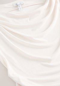Tessuto bianco drappeggiato composto da un materiale leggero e morbido, con pieghe delicate e una leggera lucentezza. Etichetta di cura visibile nella parte superiore.