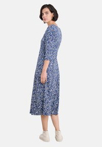 Niebieska midi sukienka w kwiaty z rękawami o długości trzy czwarte, z białym wzorem liści, luźny krój, w zestawie z jasnobrązowymi botkami za kostkę.