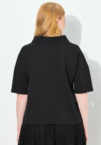 Top negro de manga corta con un corte relajado y un cuello alto, que presenta una textura suave y un diseño minimalista.