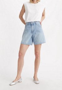 Denim shorts in light blue with a high waist and straight-cut legs, paired with a white sleeveless top and silver flat shoes.