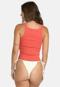 Top de tirantes estrechos de canalé de color coral, combinado con un bikini de braguitas blancas ajustables. Tono de piel visible en la espalda de la modelo.