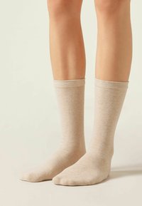 Beiga knästrumpor i midjelängd med en slät konsistens, med en muddkant upptill och en stängd tådesign, placerade på bara ben.