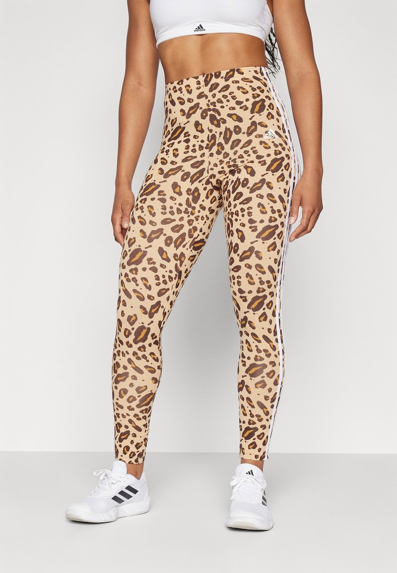 Högmidjade leggings med leopardmönster i beige med bruna fläckar, med vita sidostråkar och i kombination med vita sportskor.