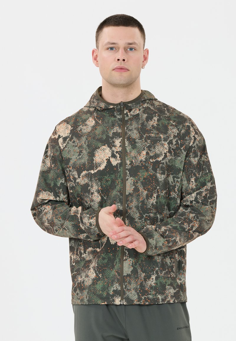 Kamik-mönstrad zip-up jacka i gröna, bruna och orange detaljer. Tillverkad av ett strukturerat tyg med en åtsittande huva och elastiska ärmslut.