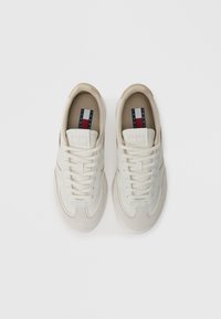 Białe sneakersy z beżowymi zamszowymi akcentami, gładką skórą i materiałami syntetycznymi, z sznurowanym zapięciem i logo marki na języku.