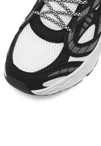 Zapatilla en blanco y negro con parte superior de malla, suela de goma y acentos texturizados con un diseño de cordones con patrón para un soporte mejorado.