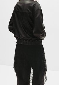 Czarna kurtka z sztucznej skóry o luźnym kroju, z elastycznym paskiem w talii i gładką fakturą. Koronkowe wykończenie u dołu dodaje kontrastu i wizualnego zainteresowania.