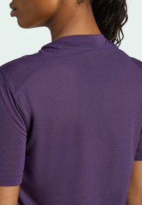 Camisa atlética morada con una parte posterior de malla texturizada, mangas cortas y un cuello bajo; tejido ligero y transpirable para mayor comodidad durante la actividad.