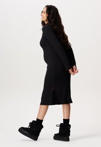 Schwarzes, geripptes Midikleid mit langen Ärmeln und Seitenschlitzen, kombiniert mit schwarzen, klobigen Plattformstiefeln mit einer weichen, strukturierten Oberfläche.