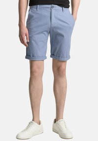 Lichtblauwe katoenen shorts met opgerolde omslagen, voorzakken en een knoopsluiting, gecombineerd met witte sneakers. Minimalistisch ontwerp.