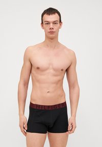 Crne bokserice s bordo pojasom na kojem je ispisano "HILFIGER" crnim tekstom. Tkanina izgleda glatko i rasteže se oko struka.