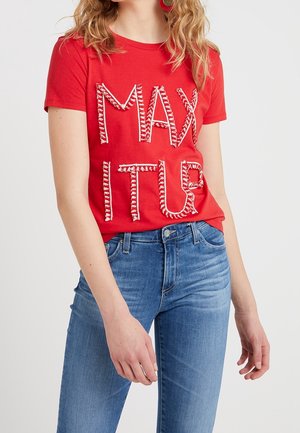Red cotton t-shirt featuring raised white lettering spelling "MAX ITUR." Paired with blue denim jeans, the shirt has a crew neckline and short sleeves.