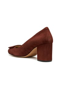 Zapato de tacón alto de ante marrón con punta redonda, un lazo decorativo en la parte delantera y un tacón grueso que proporciona soporte.