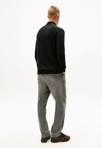 Suéter negro de punto con cuello de canalé, combinado con jeans de mezclilla gris claro. El atuendo se completa con zapatillas texturizadas en negro y rojo.