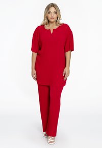 Rode geribbelde top met een keyhole halslijn gecombineerd met bijpassende geribbelde broek. Het ontwerp heeft een losvallende pasvorm en korte mouwen.