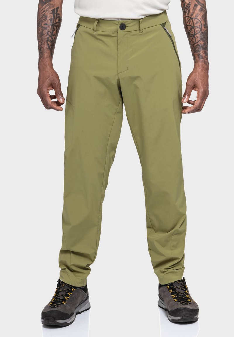 Grüne Outdoor-Hosen aus wasserabweisendem Material, mit einer lässigen Passform, Reißverschlusstaschen und verstärkten Nähten. Kombiniert mit grauen Wanderschuhen.