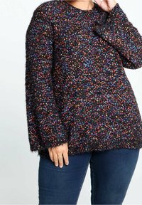 Svart texturerad tröja med flerfärgade fläckar, rund halsringning, långa ärmar och en löst sittande passform. Tyget verkar mjukt och mysigt.