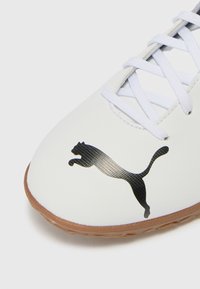 Hvit sneaker med teksturert finish, gummisåle og svart Puma-logo. Har hvite lissser og et rundt tådesign.