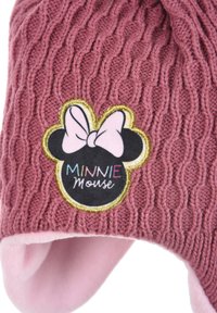 Cappello rosa lavorato a maglia con motivo a treccia. Presenta una toppa circolare nera con il testo "MINNIE Mouse" e un accento a forma di fiocco rosa. Fodera interna morbida di colore rosa.