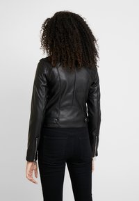 Svart motorcykeljacka i läder med en figursydd design, hög krage, dragkedjor vid ärmsluten och synliga söm detaljer.