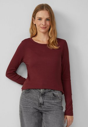 Bordeaux lang mouwtop van ribstof, met een ronde halslijn en een klein logo op de borst, gecombineerd met grijze jeans.