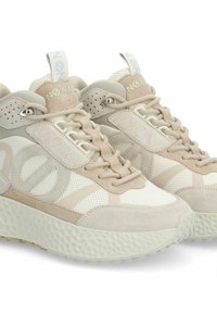 Sneakers beige con una combinazione di mesh e suede, suola testurizzata, punta arrotondata e un'impugnatura sul tallone. Gli accenti includono un logo sulla linguetta.