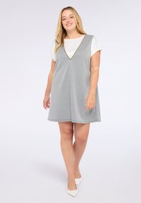 Grau-weiß karierter Kleid mit V-Ausschnitt, ärmellosem Design und einem fließenden Rock. Kombiniert mit weißen spitzen Schuhen.