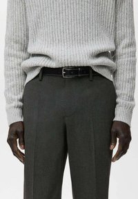 Maglione grigio a coste con maniche lunghe, abbinato a pantaloni grigio scuro e una cintura in pelle nera con fibbia argentata.