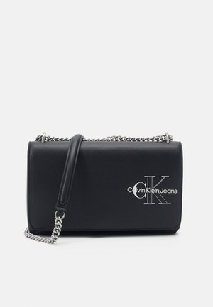 Černá kožená crossbody taška s řetízkem, s stříbrným logem "CK" a hladkým povrchem. Kompaktní obdélníkový design.