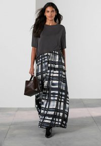 Top grigio a maniche corte abbinato a una lunga gonna con un motivo a griglia in bianco e nero. Porta una borsa a tracolla marrone scuro e indossa stivaletti neri.