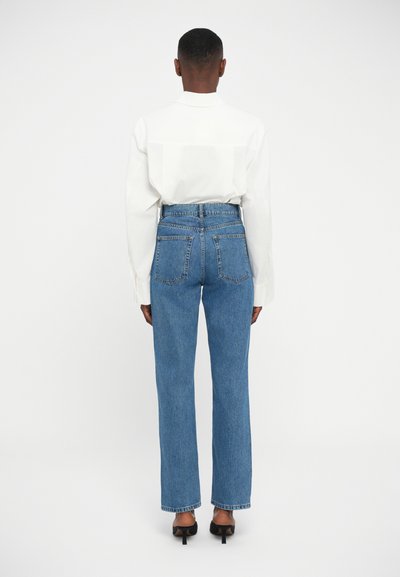Kõrge vöökohaga sinised denim teksad sirge lõikega, millel on tagataskud ja puhas äär, koos valge särgiga.