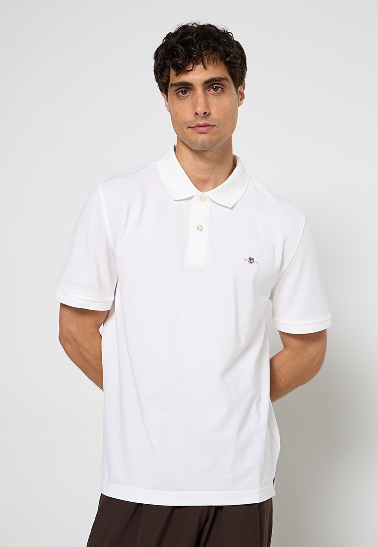 Weißes Polohemd aus Baumwolle mit klassischem Kragen, zwei Knöpfen und kleinem Logo auf der linken Brust. Kurzärmlig und mit strukturiertem Stoff.