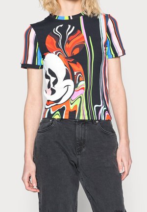 Kobieta w kolorowej, krótki rękaw w paski z dużym falistym, abstrakcyjnym nadrukiem twarzy w stylu kreskówkowym, w połączeniu z czarnymi, wysokim stanem jeansami.