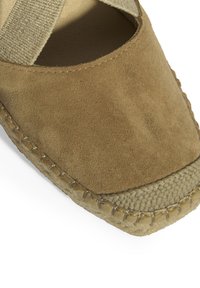 Braune Wildleder-Espadrille mit runder Zehenform, gewebter Jutesohle und überkreuzten elastischen Riemen. Glatte Textur mit genähten Details.