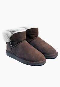 Botas recortadas de suede marrón con un suave forro de piel de oveja gris, que cuentan con una correa lateral y un detalle de hebilla, además de una suela de goma texturizada.